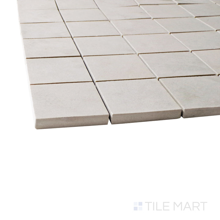 Captured from a corner angle, the Creos Cookie 2" square matte porcelain mosaic tile showcases its warm beige hue and precise square layout, adding subtle texture and elegance to surfaces.