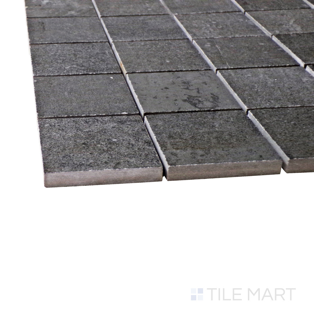 Captured from a corner angle, the Ecocrete Weathered Black 2" square matte porcelain mosaic tile showcases its deep black shade and structured design, adding a modern and industrial touch to accent walls and floors.