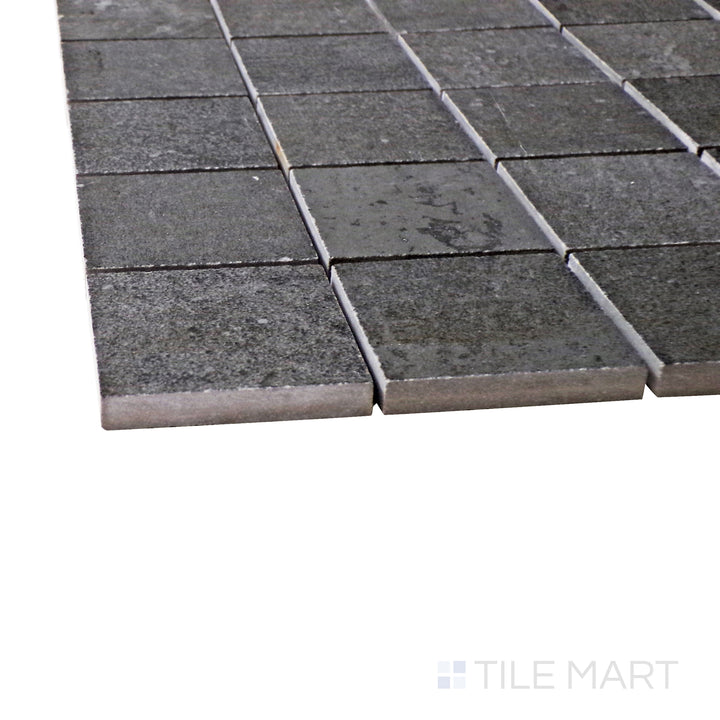 Captured from a corner angle, the Ecocrete Weathered Black 2" square matte porcelain mosaic tile showcases its deep black shade and structured design, adding a modern and industrial touch to accent walls and floors.