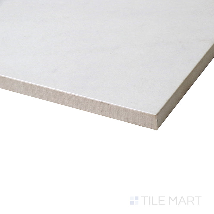 A side-angle shot highlights the smooth, polished surface of this Lugano Marfil porcelain tile, reflecting soft beige tones with subtle veining.
