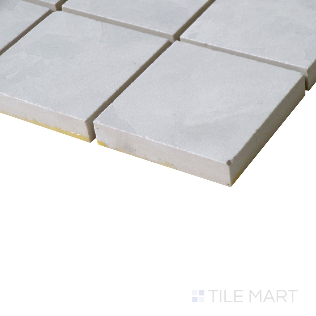 Slanted perspective of Tele Di Marmo Revolution Thassos 2" Square matte porcelain mosaic, emphasizing its pure white tones, smooth texture, and geometric square pattern.  