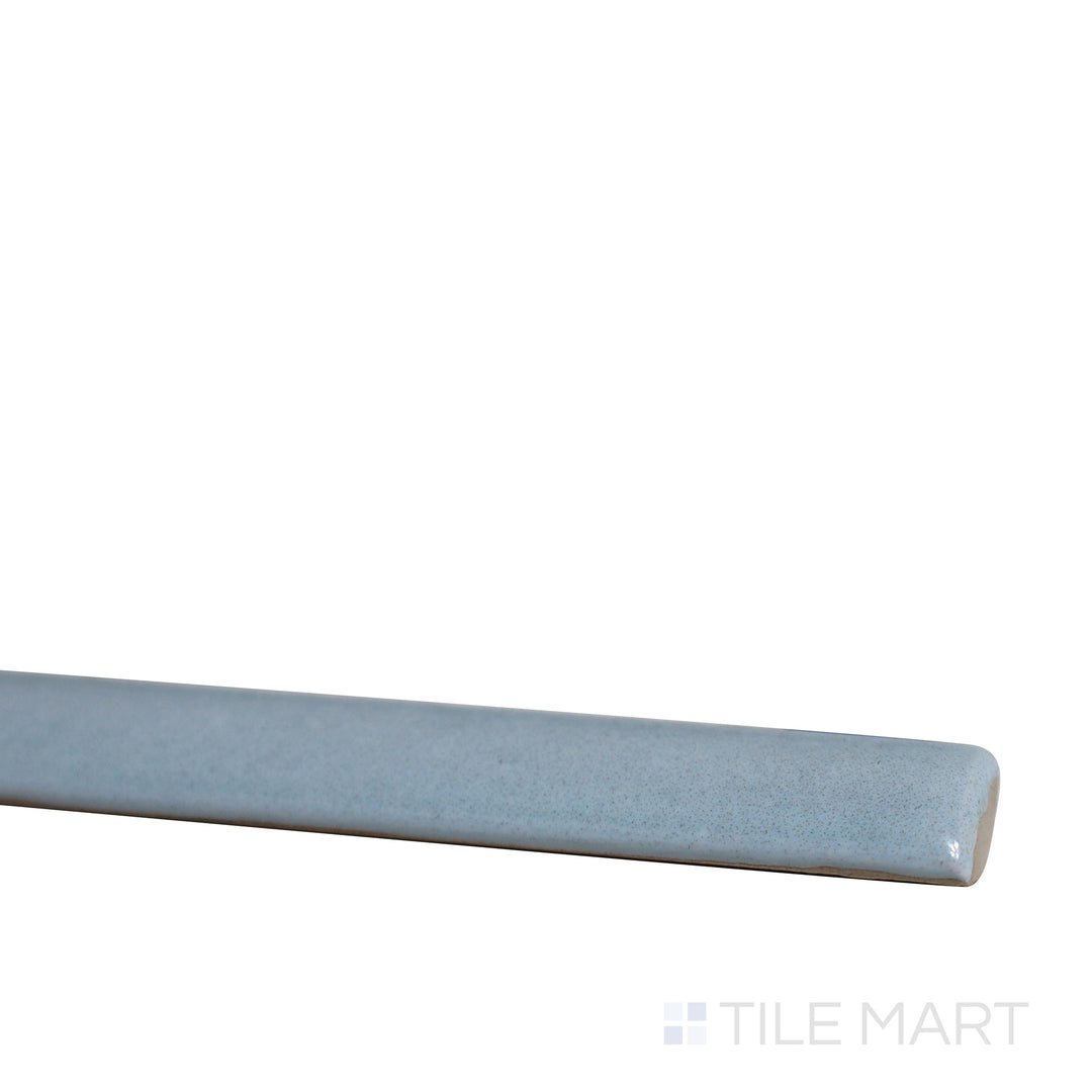 Slanted perspective of Village Cloud 0.5x8 glossy ceramic jolly tile, emphasizing its soft gray-blue tone, smooth polished texture, and structured trim format.  