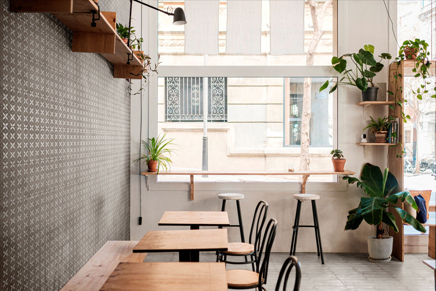 Modern cafe interior with wooden tables, chairs, and plants, featuring Amuri Brick Grigio 2x12 Matte Porcelain Tile to create a sleek, neutral foundation.