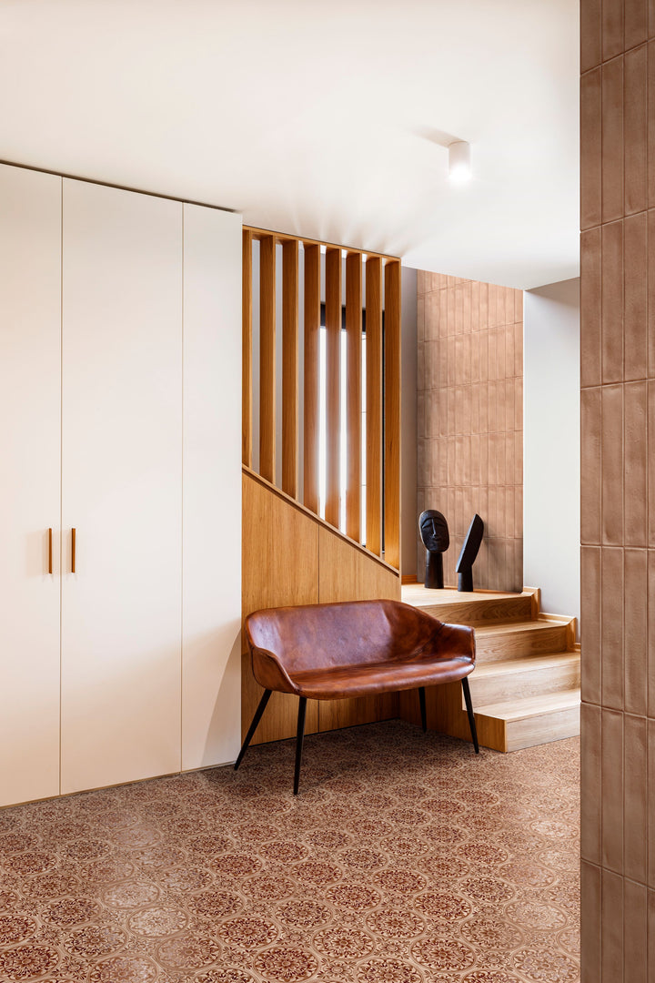 Modern interior with brown leather chair, wooden staircase, and white walls, grounded by Amuri Decoro Pizzo Cotto 8x8 Matte Porcelain Tile for a warm, textured accent.