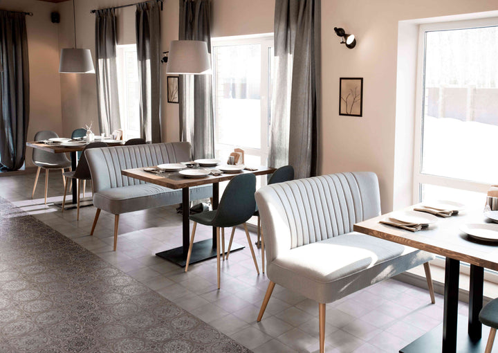 Modern dining area with tables, chairs, and a bench in a well-lit room, featuring Amuri Decoro Pizzo Grigio 8x8 Matte Porcelain Tile to add soft pattern and contrast.
