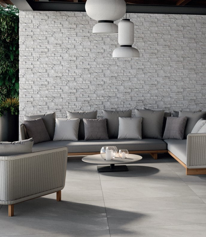 Gray sofa set with cushions positioned against a light gray brick wall, grounded by Hurricane Silver 24x48 Matte Porcelain Tile in a sleek, neutral finish.