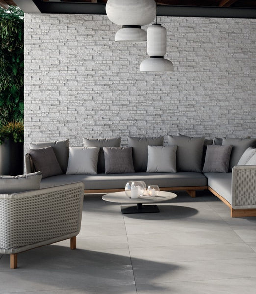 Gray sofa set with cushions positioned against a light gray brick wall, grounded by Hurricane Silver 24x48 Matte Porcelain Tile in a sleek, neutral finish.