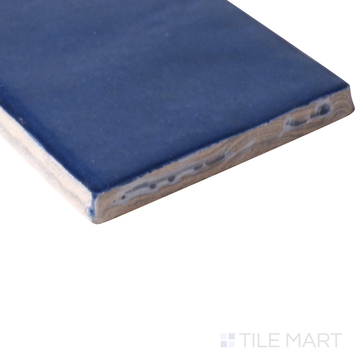 Angled perspective of Cloe Blue 2.5x8 gloss glazed ceramic tile, highlighting its rich blue shade, reflective surface, and sharp edge detailing at the corner.