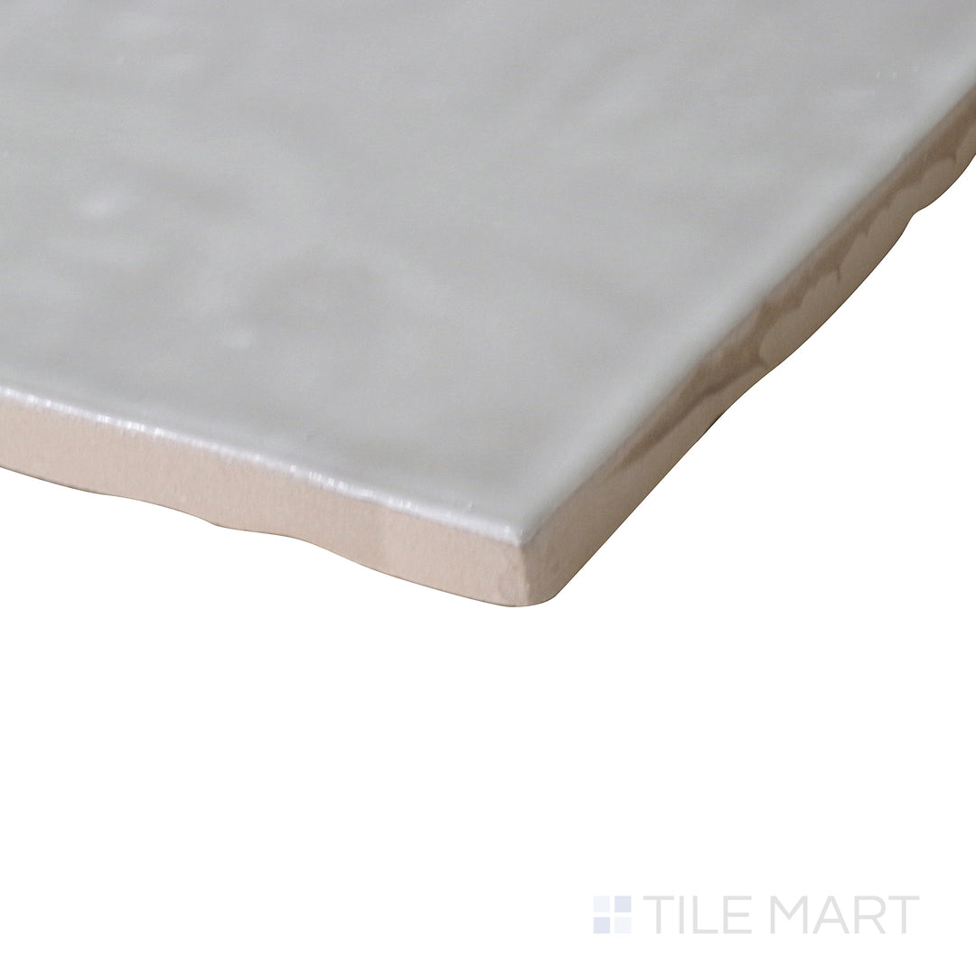 Angled view of Marin Pebble Gray 4x4 gloss glazed ceramic tile, showcasing its muted gray hue, polished finish, and how the light interacts with the glossy surface at the corner.