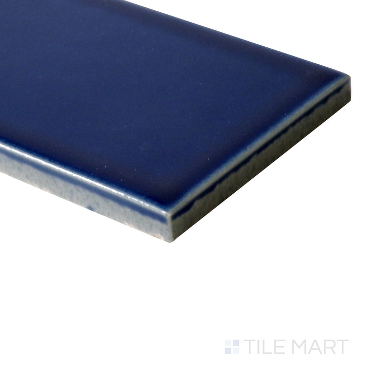 Angled perspective of Zenia Tide 2.5x9 gloss glazed porcelain tile, showcasing its deep ocean blue shade, high-gloss sheen, and the smooth connection at the corner.