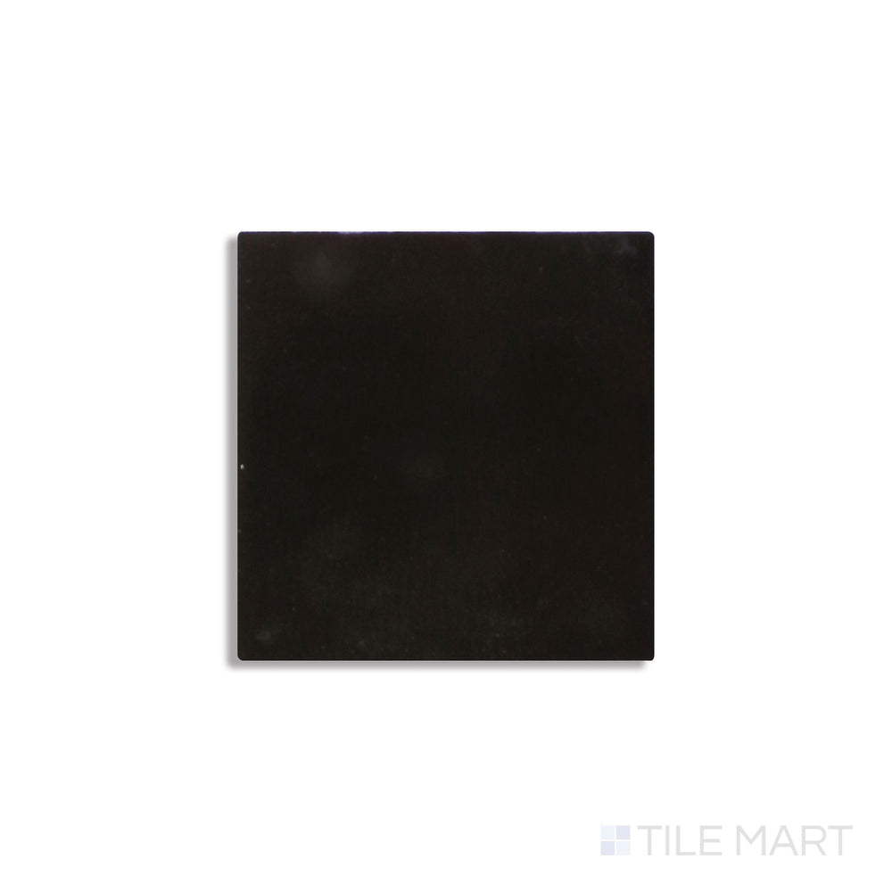 Angled view of Zellige Neo Carbone 4x4 glossy glazed ceramic tile reveals rich dark tone and reflective handcrafted surface.