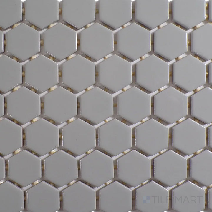 The overhead perspective highlights the Color Wheel Mosaic Desert Gray 1.5" hexagon glossy glazed ceramic tile, featuring a neutral gray tone with a reflective surface that enhances light and depth in designs.