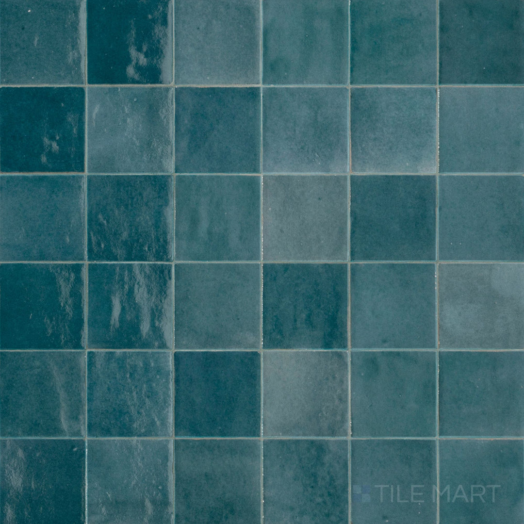 Top-down view of Zellige Neo Petrolio 4x4 glossy glazed ceramic tile, highlighting its rich blue-green hue and handmade texture.
