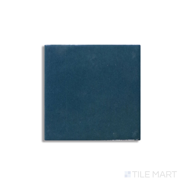 Zellige Neo Petrolio 4x4 glossy glazed ceramic tile seen at an angle, highlighting its deep hue and wavy, reflective surface.