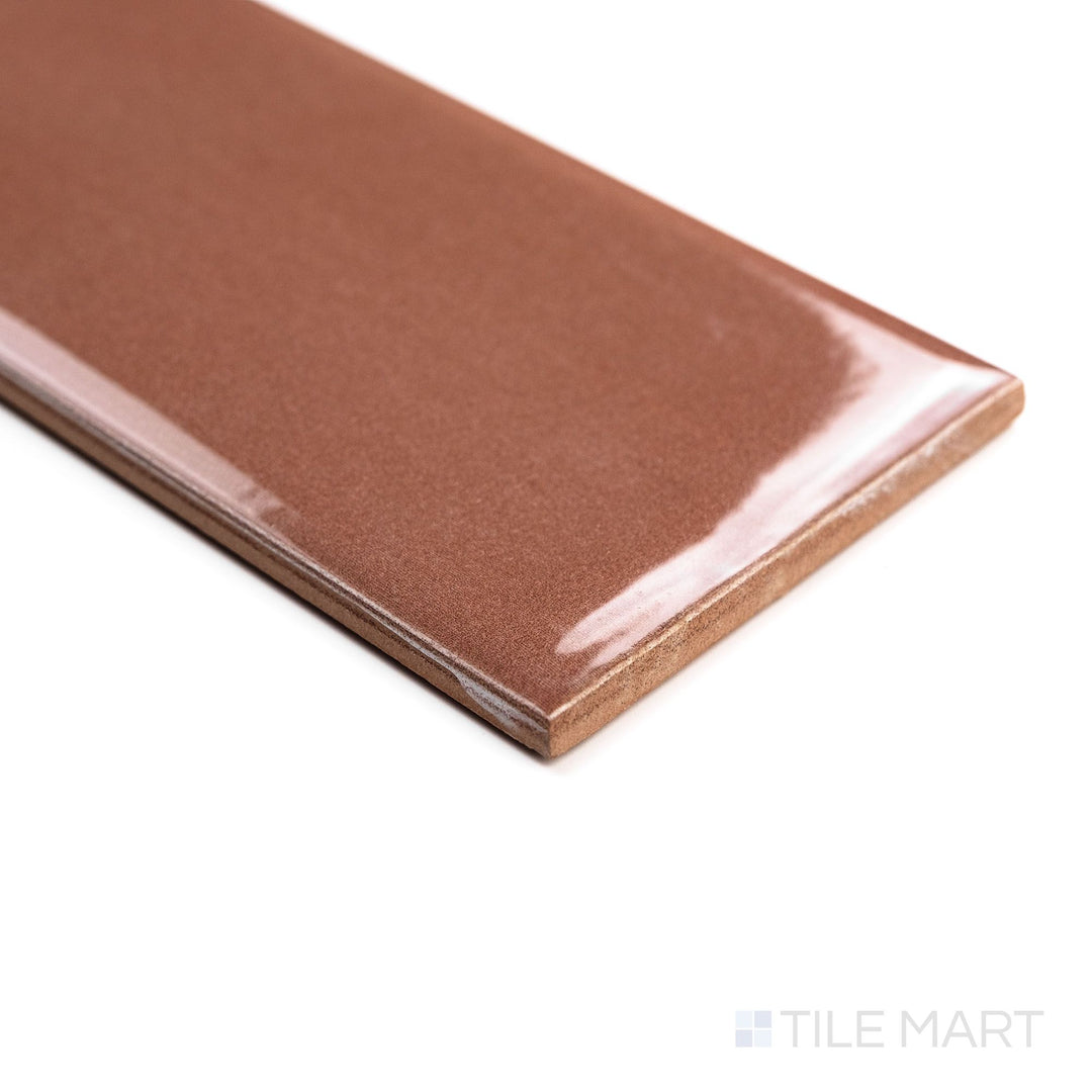 Angled view of Canvas Red Bean 3x10 Glossy Ceramic Tile showing its rich red glaze and reflective finish with subtle light play across the surface.