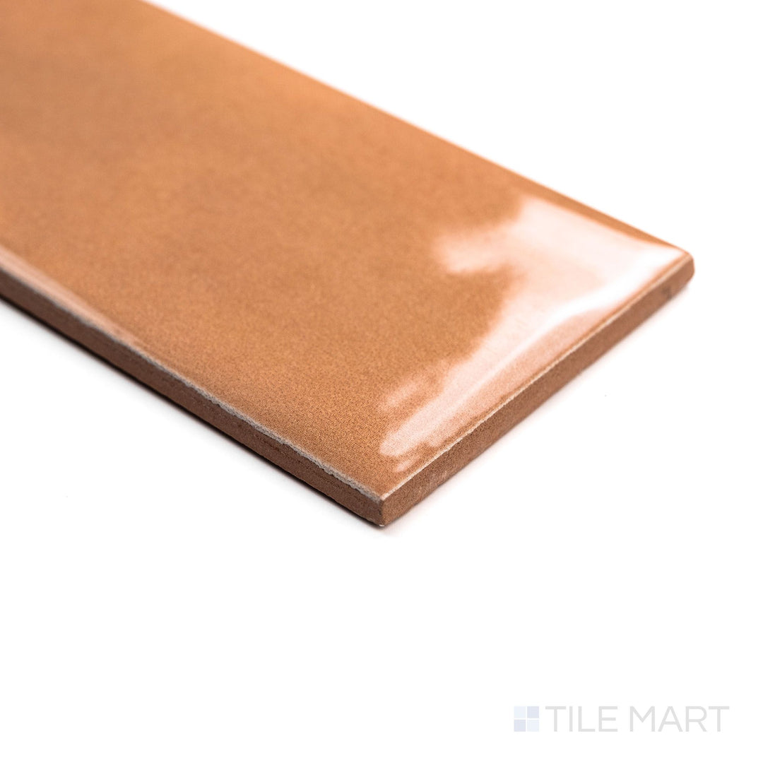 Canvas Orange Peel 3x10 Glossy Ceramic Tile in an angled shot, displaying its vivid orange hue and slick glossy coating with a dynamic visual effect.