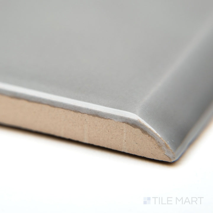 A corner-focused shot of Block Acero 2x10 bright ceramic bullnose, featuring a soft steel-gray hue with a polished, reflective surface.