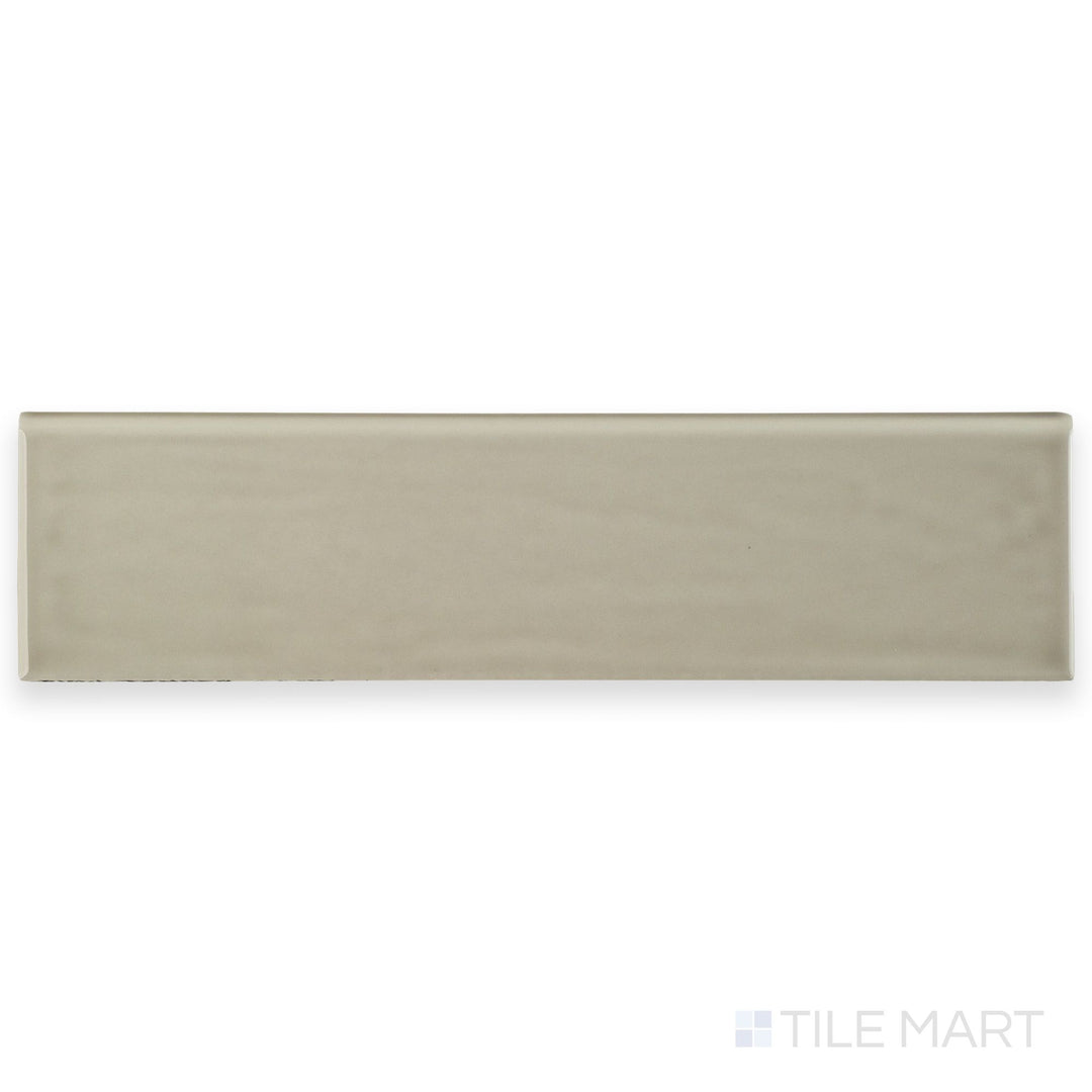 This image displays Flow Tender Gray 3x12 Bright ceramic bullnose tile, emphasizing its soft gray tone, glossy surface, and rounded edge.