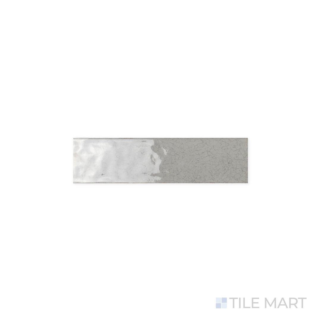 A close-up view of Maiolica Tender Gray 3x12 Bright Ceramic Tile, showcasing its polished surface and soft gray tone. The glossy finish enhances light reflection for a refined, sleek look.
