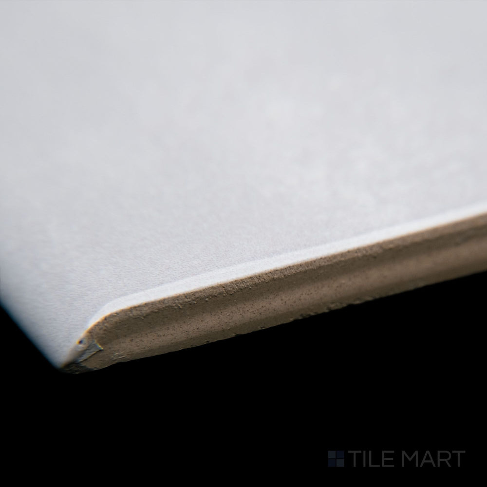 A corner-focused shot of Maiolica Tender Gray 3X10 bright ceramic bullnose, capturing its neutral gray color, gently curved edge, and glossy ceramic finish.