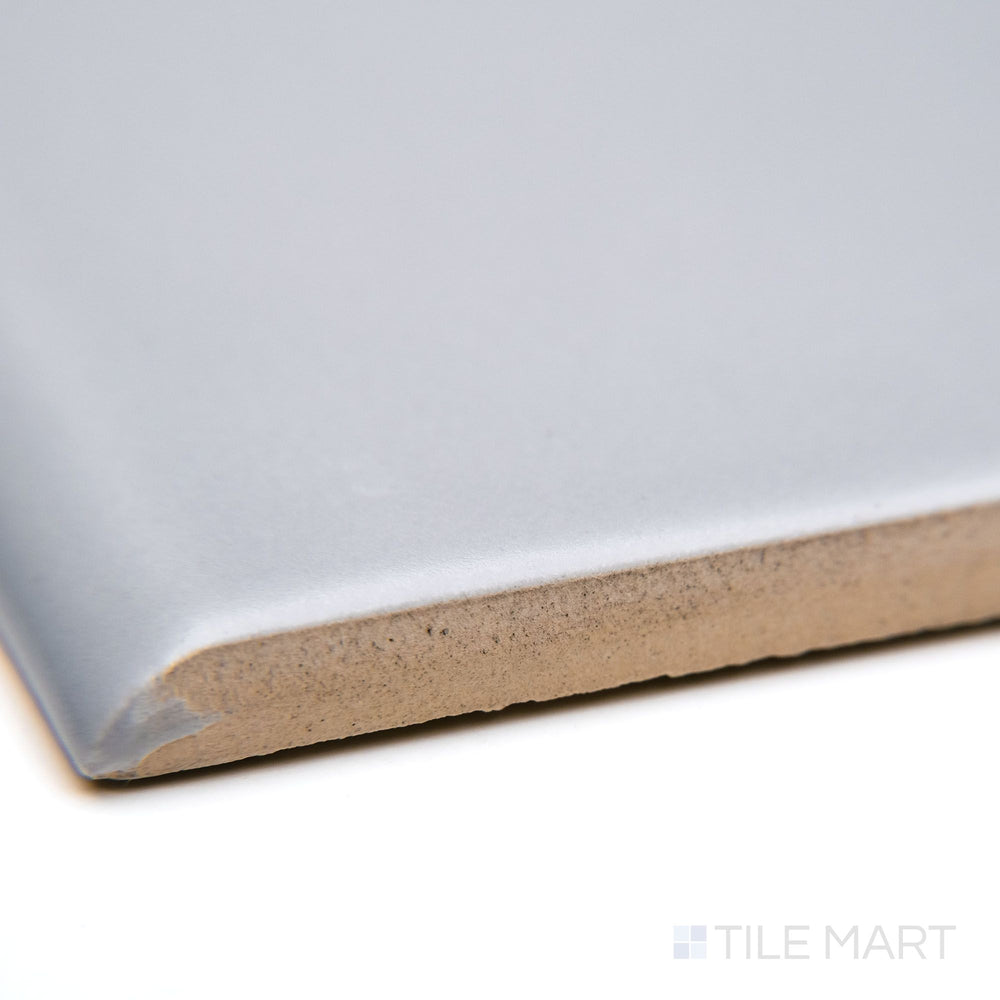 A corner-focused shot of Maiolica Tender Gray 3X10 matte ceramic bullnose, emphasizing its subtle gray shade, smooth bullnose edge, and soft matte texture.
