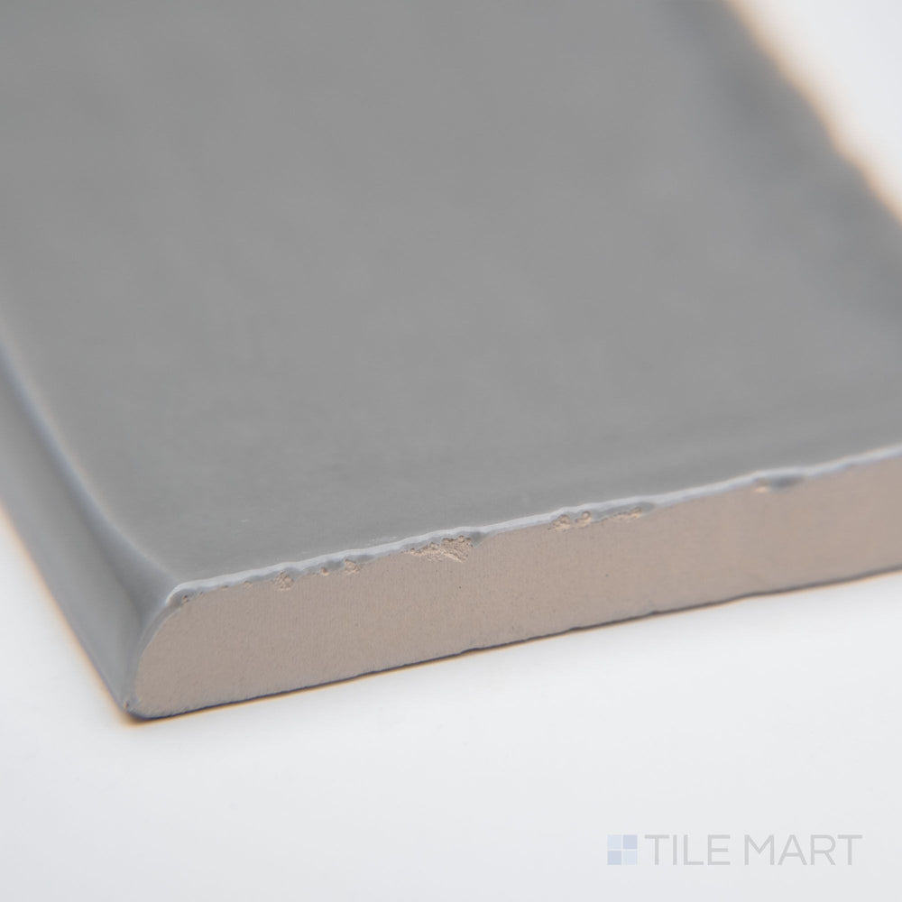 A close-up of St. Tropez Gris 2.5x5 bright ceramic bullnose, featuring a soft gray shade, polished curved edge, and sleek glossy finish.