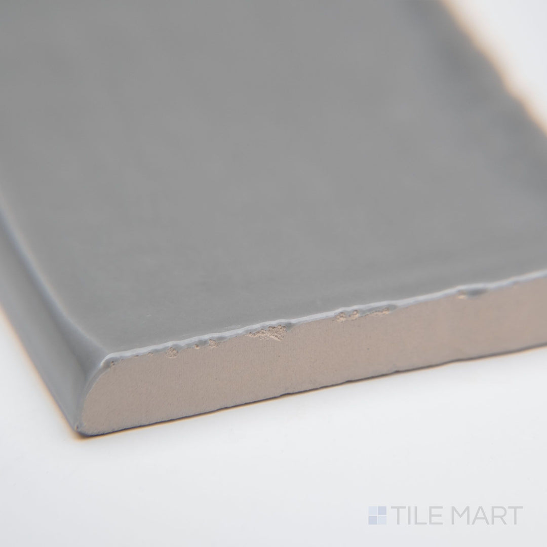 A close-up of St. Tropez Gris 2.5x5 bright ceramic bullnose, featuring a soft gray shade, polished curved edge, and sleek glossy finish.