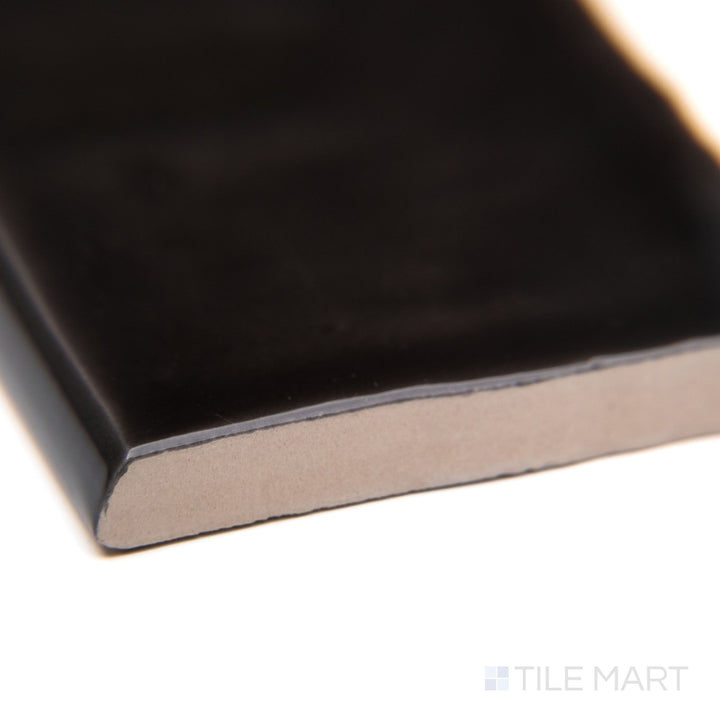 A corner-focused shot of St. Tropez Bronce 2.5x5 bright ceramic bullnose, emphasizing its warm bronze hue, smooth rounded profile, and shiny ceramic texture.