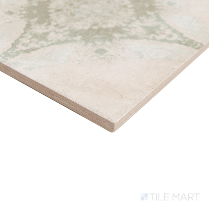 A close-up of a square ceramic tile showing its textured surface and corner edge, featuring a distressed pattern in beige and muted sage green.