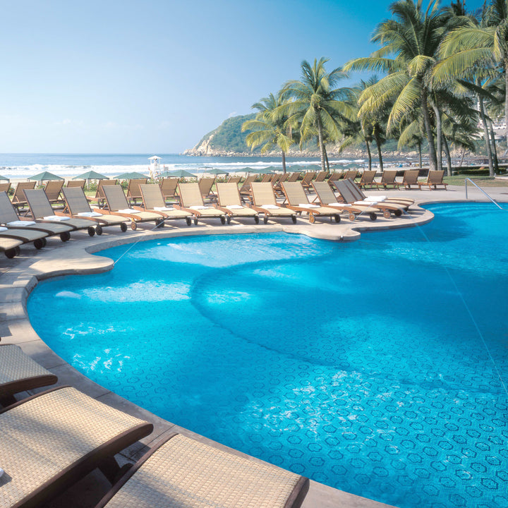 Pool area with lounge chairs and palm trees by the ocean