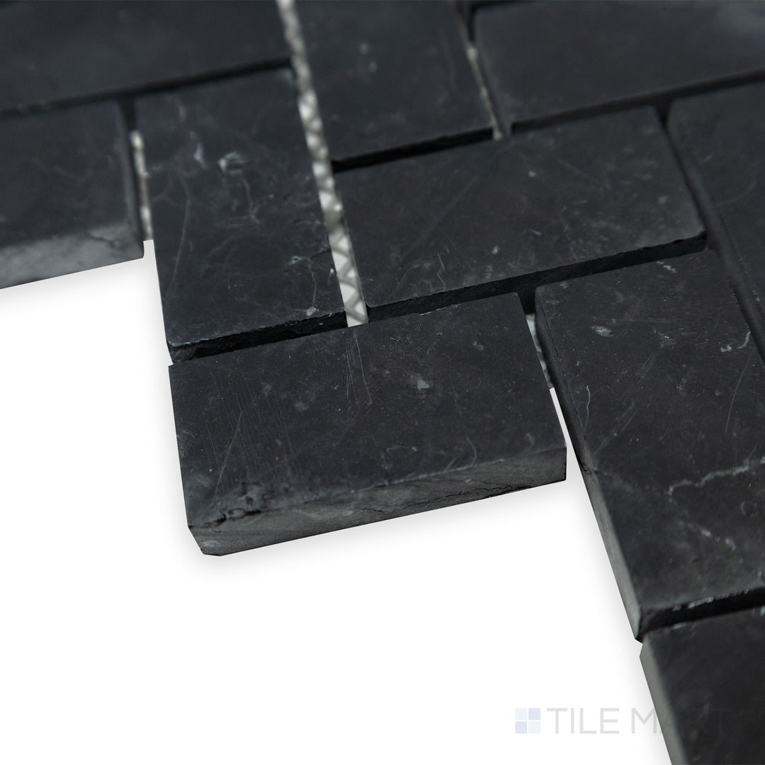 From a dynamic side angle, the flowing herringbone pattern of Negro Marquina Marble 1x2 herringbone honed mosaic is highlighted, showcasing its matte finish and crisp geometry.