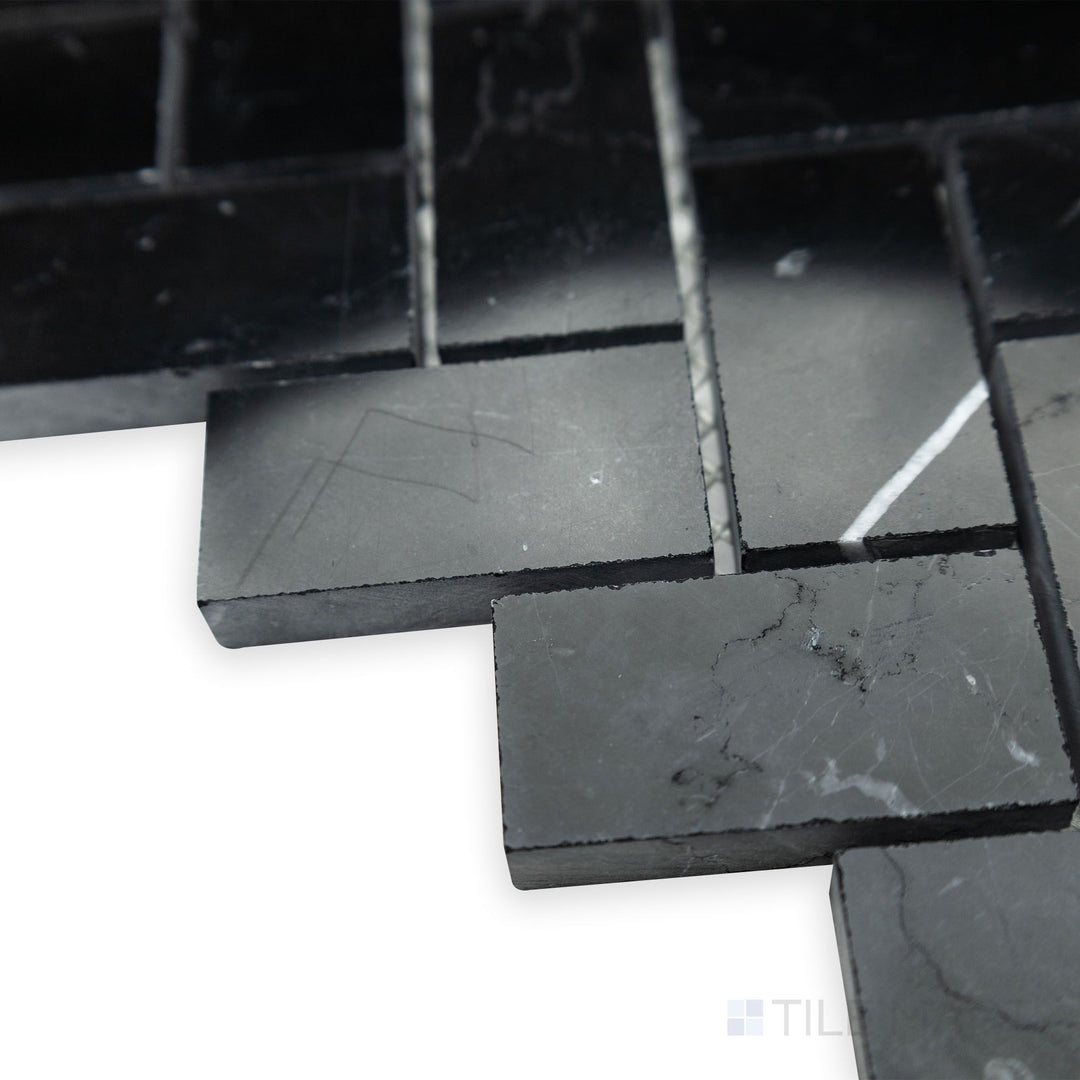 A reflective polished surface takes center stage in this corner shot of Negro Marquina Marble 1x2 herringbone polished mosaic, accentuating the tile’s elegant V-shaped pattern.