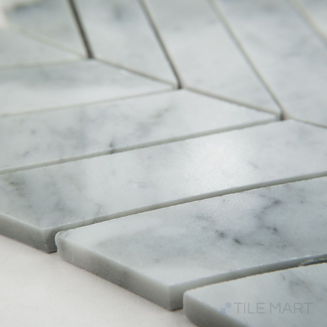Tile shown from corner angle of White Carrara Marble 1x4 chevron polished mosaic featuring sleek glossy marble in dynamic V-shaped patterns
