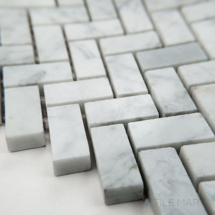 Tile corner display of White Carrara Marble 5/8x1-1/4 herringbone polished mosaic highlighting shiny marble tiles in a dynamic V pattern