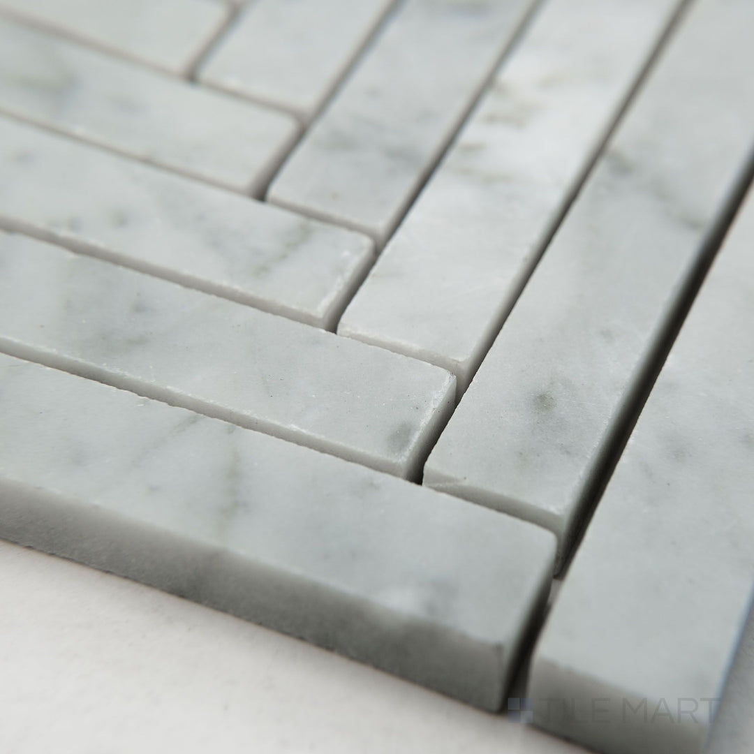 Tile shown from corner angle of White Carrara Marble 5/8x6 herringbone honed mosaic showcasing matte marble in a stylish herringbone layout