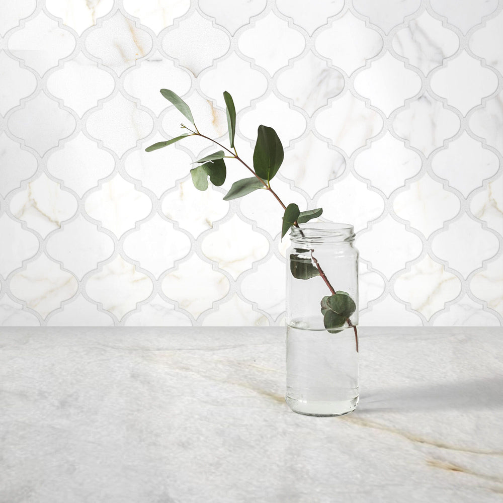Clear glass vase with a branch of eucalyptus against a white marble backsplash.