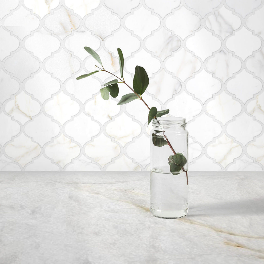 Clear glass vase with a branch of eucalyptus against a white marble backsplash.