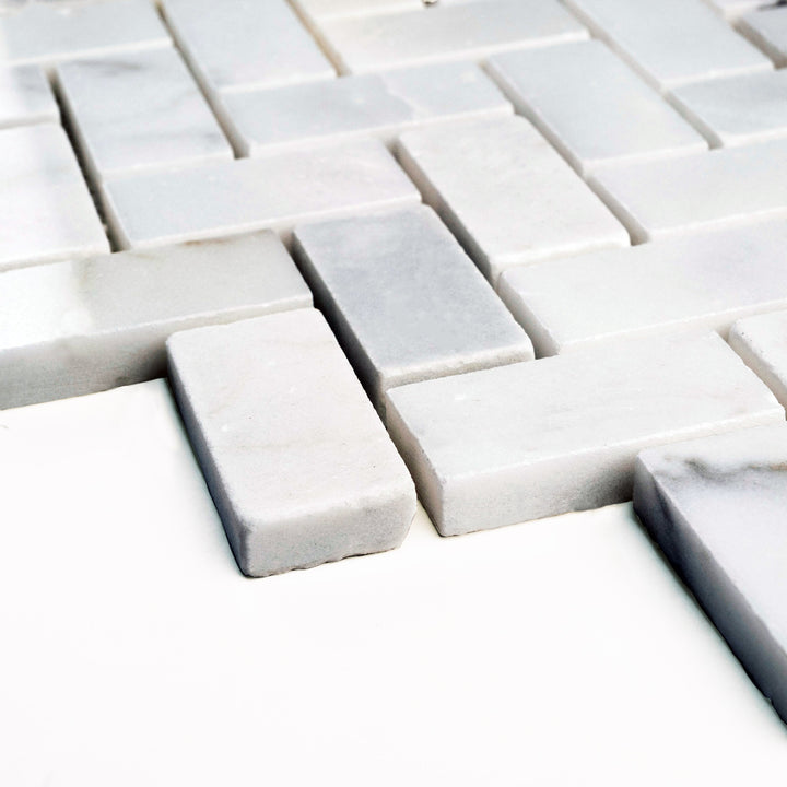 Polished Calacatta Gold 1x2 herringbone mosaic presented at an angle, highlighting the elegant interplay of warm veining within the classic pattern.