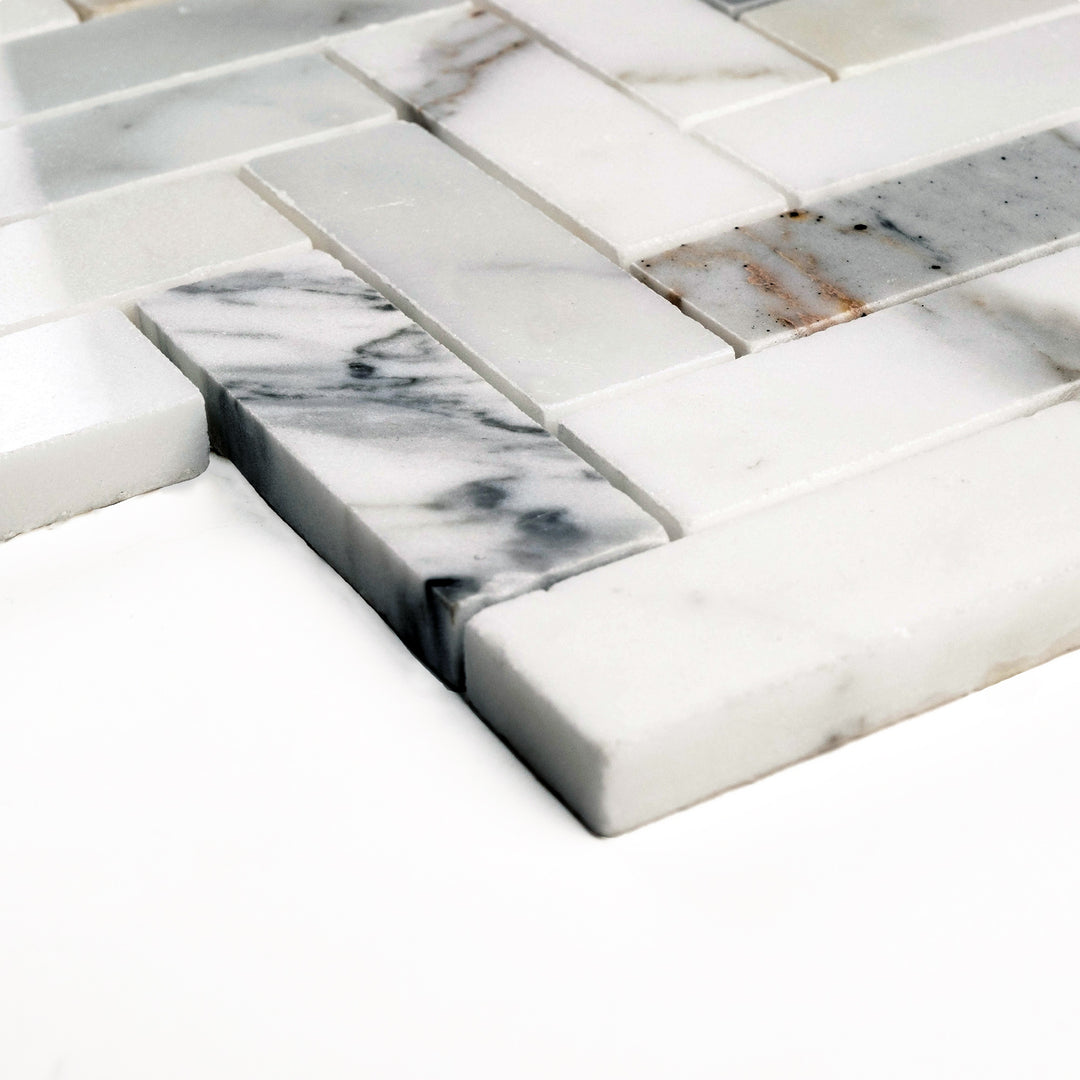 Polished 1x3 Calacatta Gold herringbone mosaic viewed from a side angle, reflecting light across its elongated pieces and rich marble veining.