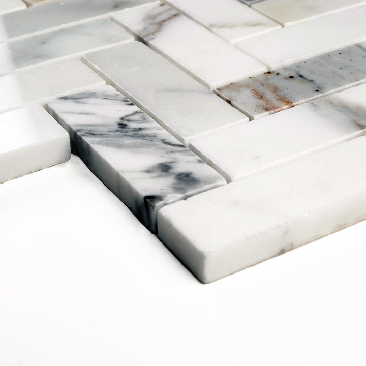 Polished 1x3 Calacatta Gold herringbone mosaic viewed from a side angle, reflecting light across its elongated pieces and rich marble veining.