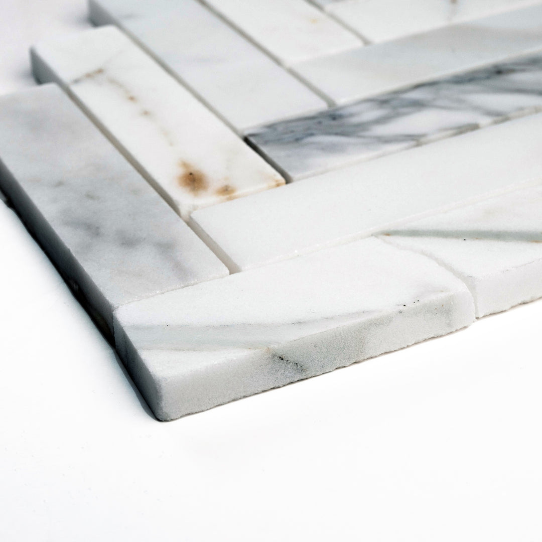 Calacatta Gold 1x4 herringbone mosaic in honed finish, photographed from a corner view to showcase its slender proportions and soft white tones.