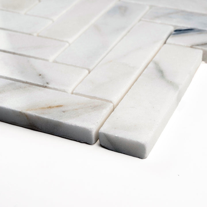 Side angle of polished 1x4 Calacatta Gold herringbone mosaic, revealing its luxurious shine and flowing golden veining across elongated tiles.