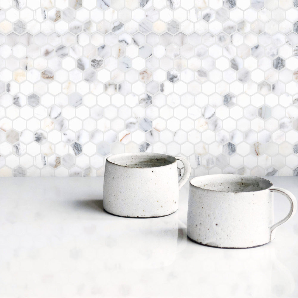 Two ceramic mugs on a white surface with a hexagonal marble tile backsplash.