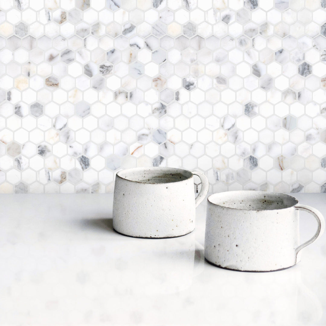 Two ceramic mugs on a white surface with a hexagonal marble tile backsplash.