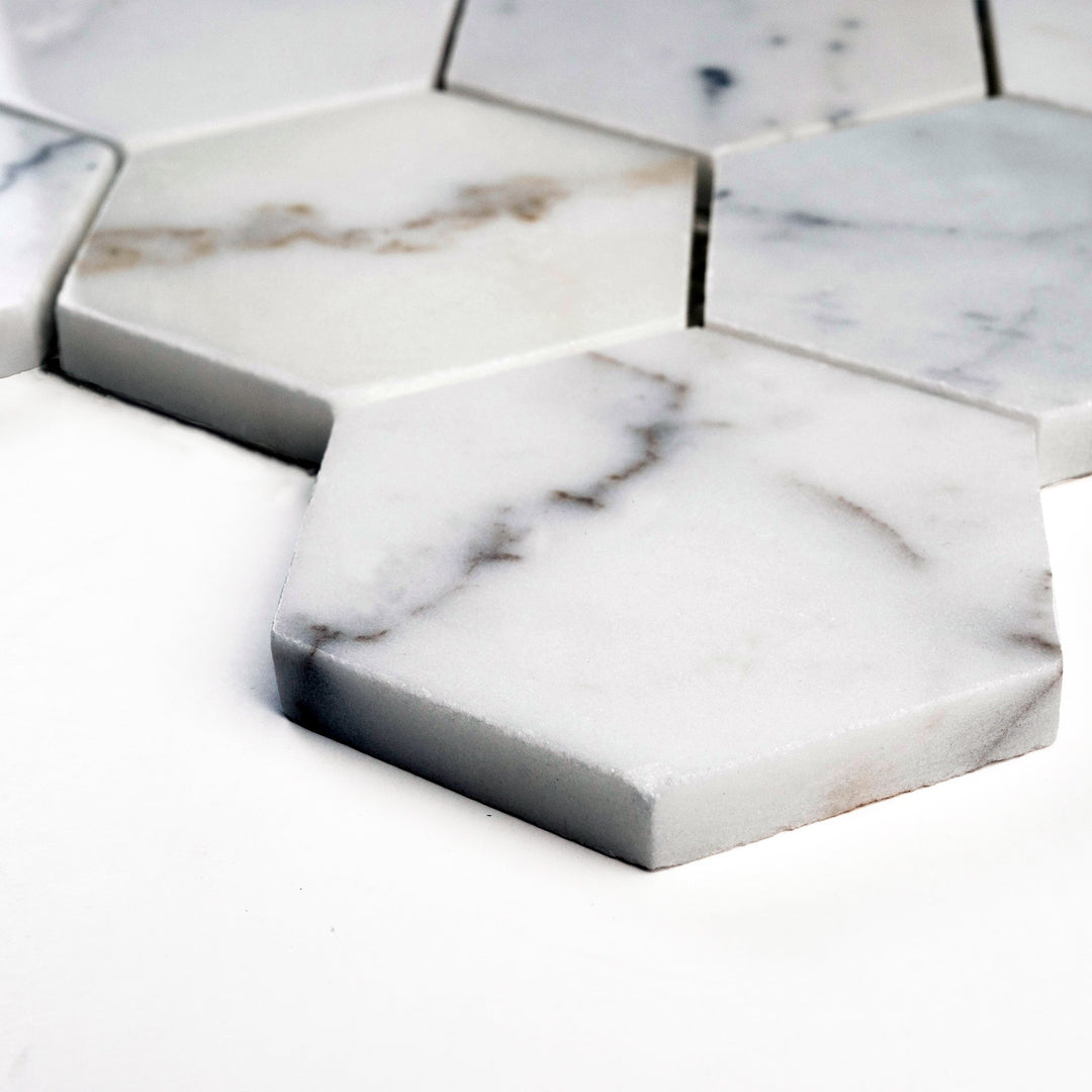 Calacatta Gold 3" hexagon polished mosaic viewed from an angle, bringing out a luminous surface and vivid natural marble movement.