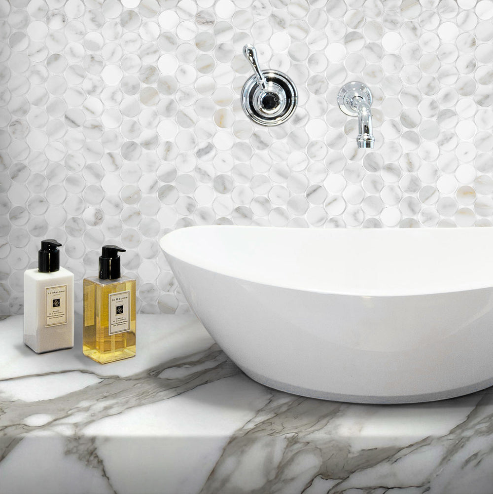 Bathroom setting with a freestanding bathtub, decorative wall tiles, and two bottles on a marble surface.