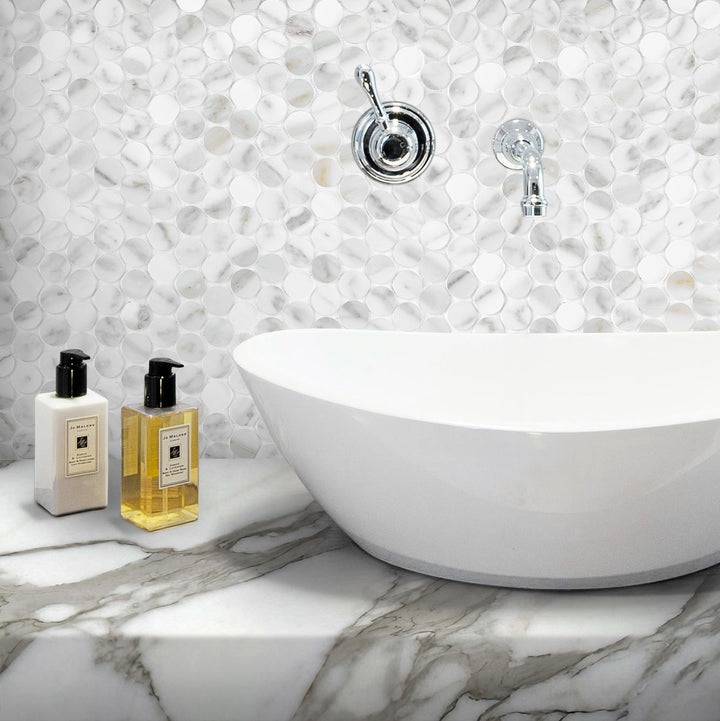 Bathroom setting with a freestanding bathtub, decorative wall tiles, and two bottles on a marble surface.