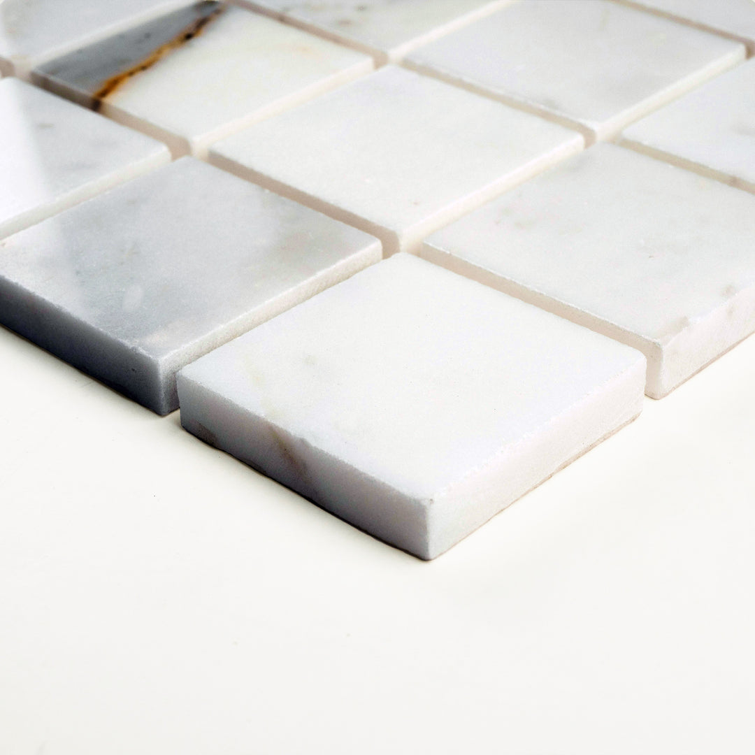 Polished 2" square mosaic in Calacatta Gold marble shown in corner shot, with bold golden patterns and mirror-like surfaces.