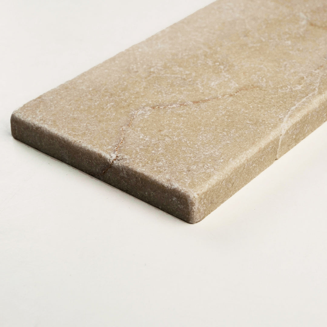 Tumbled Crema Marfil Classic 3x6 tile viewed from a side angle, offering a rustic, weathered surface with natural edge variation.