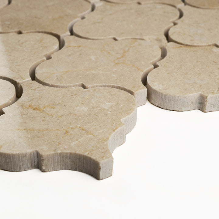Polished Crema Marfil marble in 3 inch lantern mosaic format, captured on an angle to showcase its glossy finish and classic curvature.